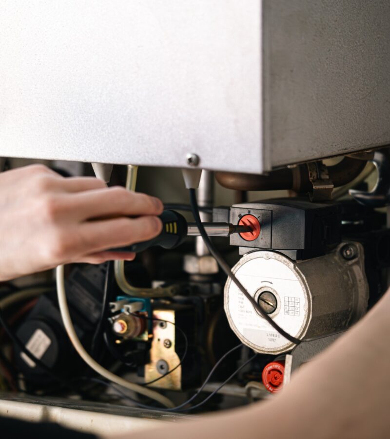 Man is repairing a heating boiler, a screwdriver and a spanner in his hands. commercial boiler servicing essex